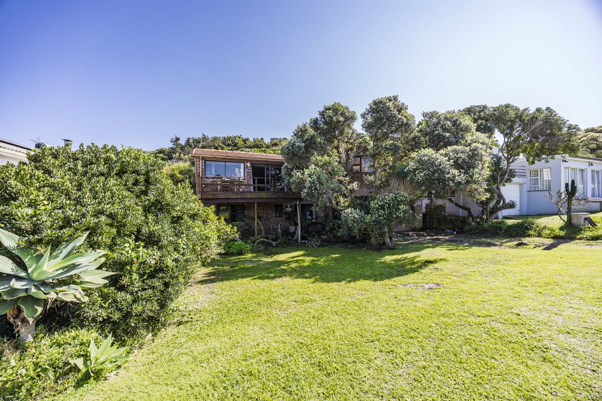 Rear view of the property featuring a raised wooden deck, brick exterior walls, and a spacious garden area with mature trees.