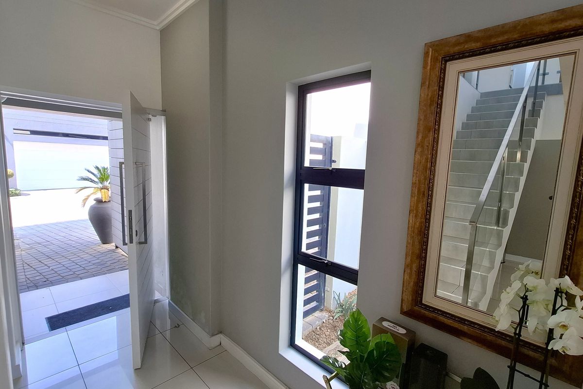 Bright entrance foyer featuring tiled flooring, a modern pivot door, and a staircase with a glass balustrade leading to the upper level.