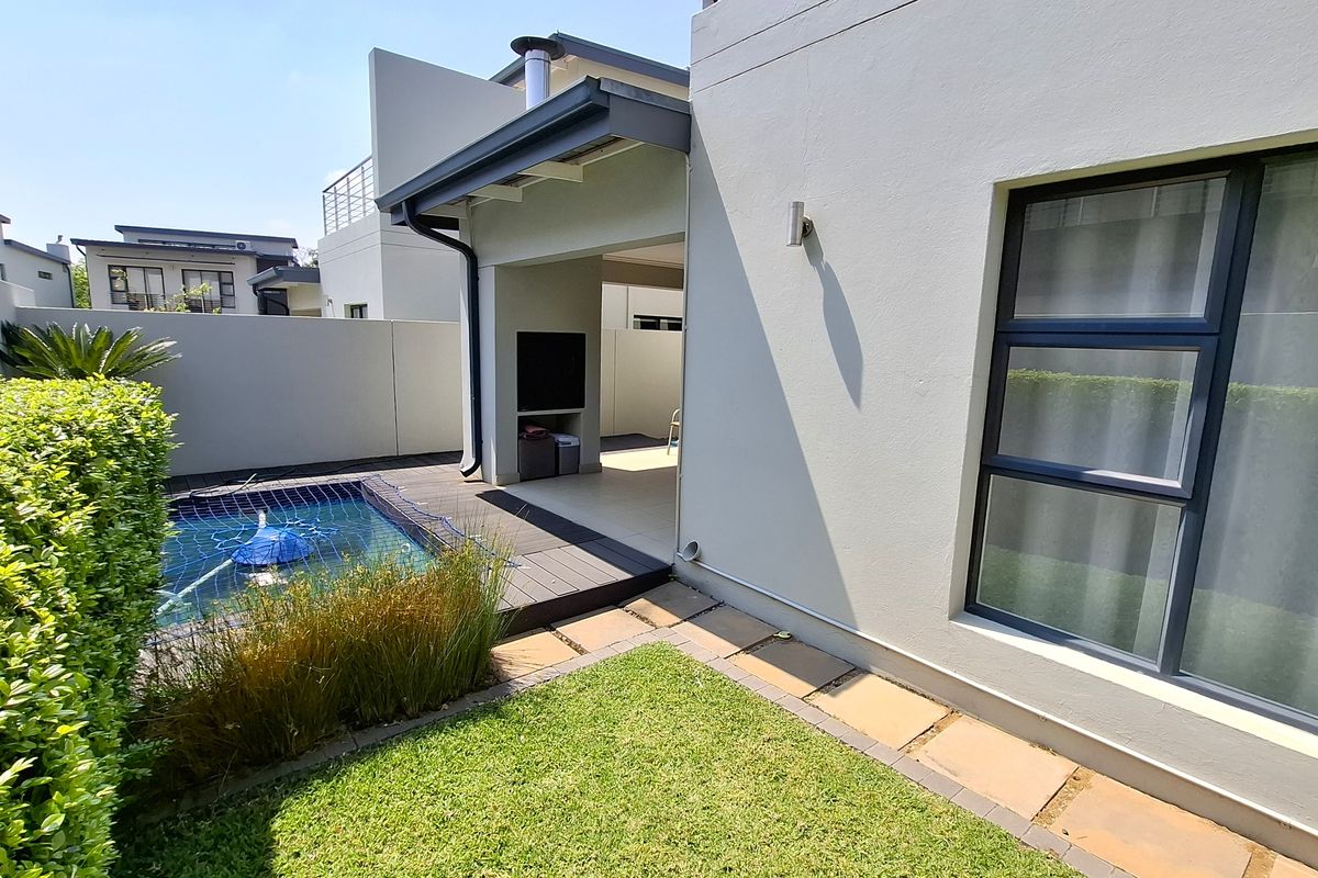 Rear exterior view featuring a covered patio with built-in braai, a small swimming pool with decking, and a well-maintained garden area.