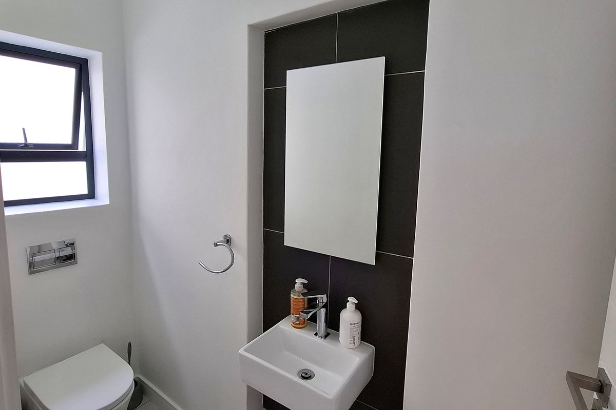A clean, modern guest bathroom featuring a wall-mounted basin, chrome fixtures, and a dark tiled feature wall.