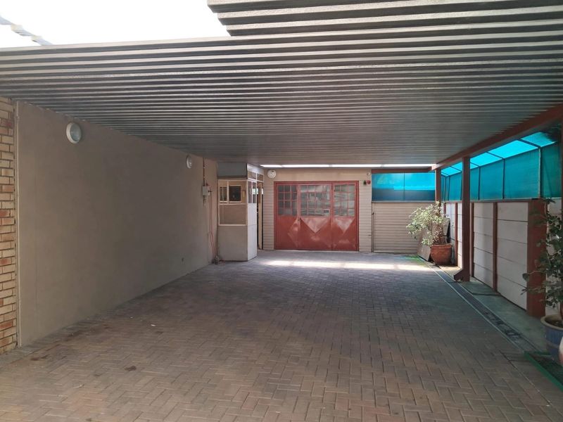 A spacious covered carport or garage area featuring paved flooring, a corrugated metal roof, and secure access doors.