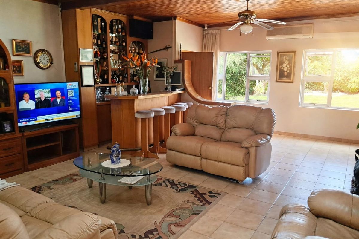 Spacious living room featuring a built-in bar, timber ceiling, ceiling fan, and split-system air conditioning, with tiled flooring and large windows overlooking the garden.