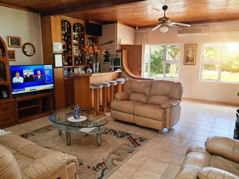 Spacious living room featuring a built-in bar, timber ceiling, ceiling fan, and split-system air conditioning, with tiled flooring and large windows overlooking the garden.