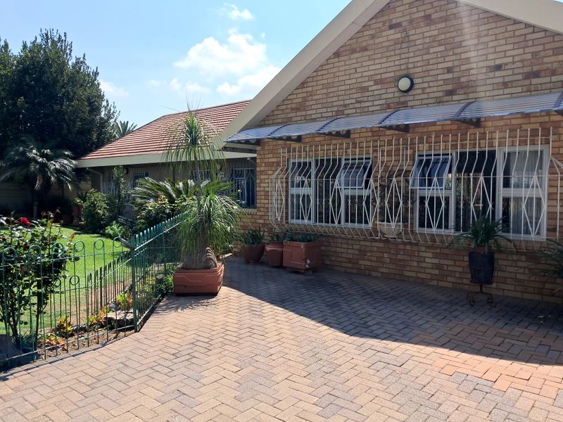A well-maintained face brick house exterior featuring a paved driveway, secure window bars, and a neat garden area.