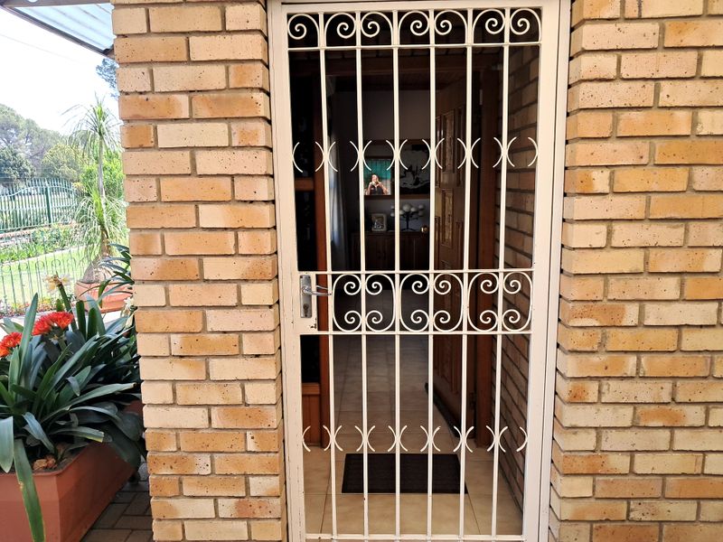 An exterior view of a home entrance featuring a brick facade and a white metal security gate.