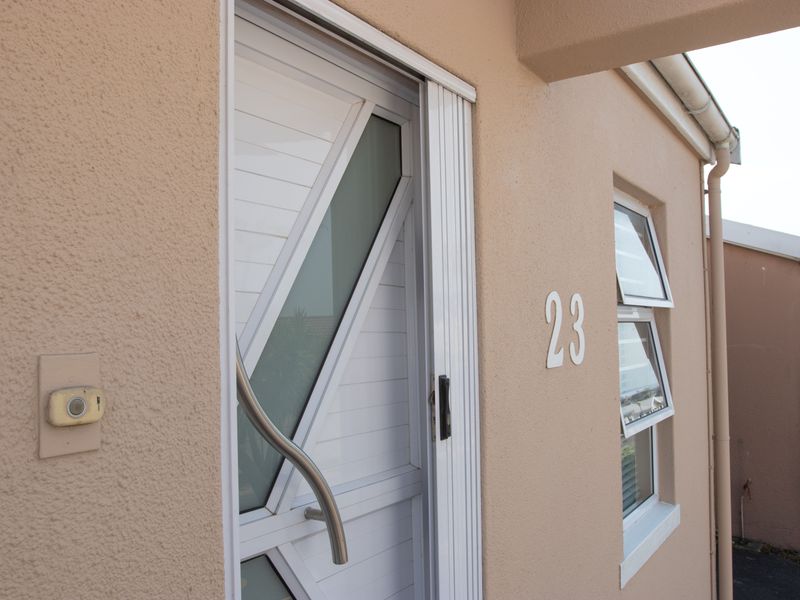 Front entrance area featuring a white security gate, awning windows, and house number 23 on a textured exterior wall.