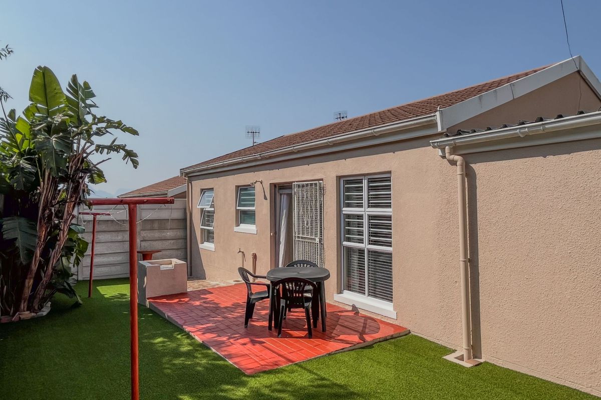 Rear exterior view featuring a paved patio area, artificial lawn, and a built-in braai, providing a low-maintenance outdoor living space.