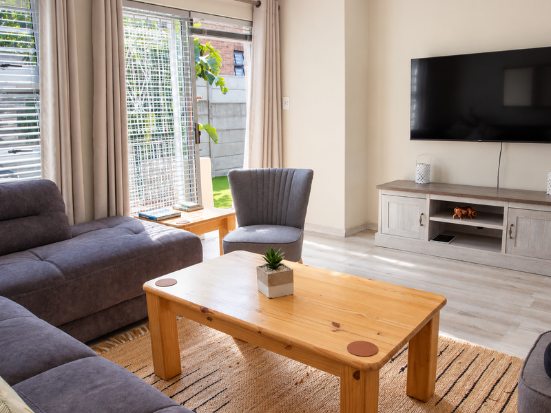 A bright and well-maintained living room featuring light laminate flooring and a large sliding glass door providing access to the outdoor area.