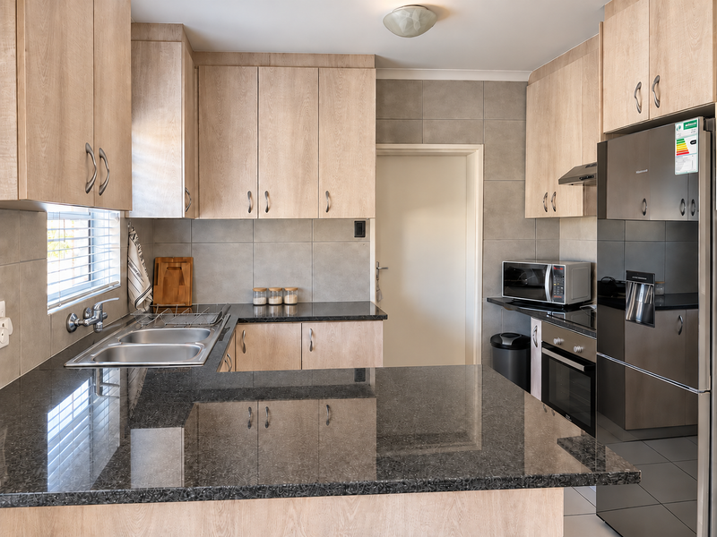 A well-maintained kitchen featuring light wood-finish cabinetry, dark granite countertops, a stainless steel sink, and integrated oven with extractor fan.