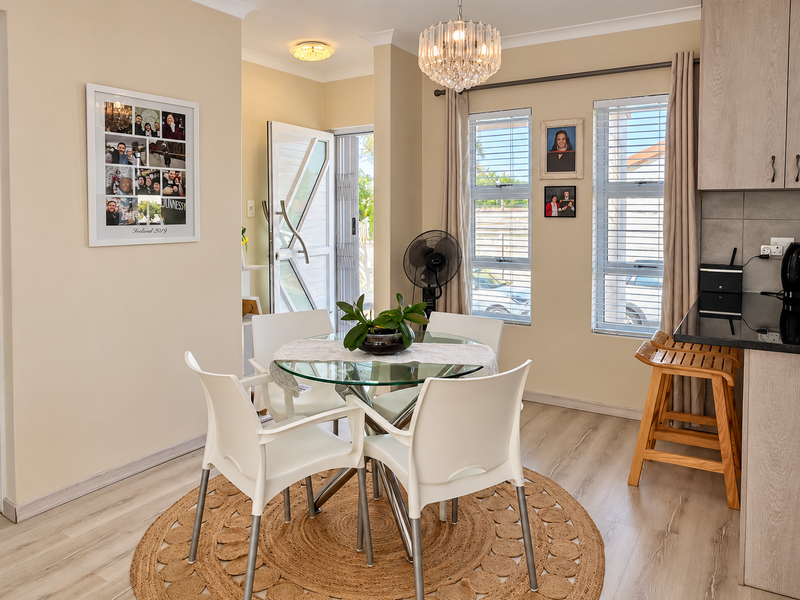 Bright open-plan dining area featuring modern laminate flooring, a stylish crystal chandelier, and direct access to the exterior through a secure entrance.
