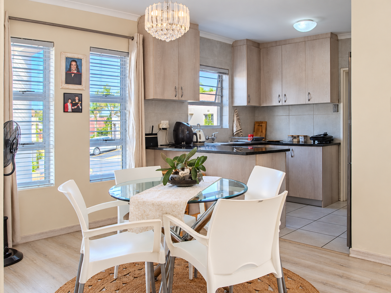 Open-plan kitchen and dining area featuring light wood-finish cabinetry, granite countertops, tiled backsplash, and a combination of laminate and tiled flooring.