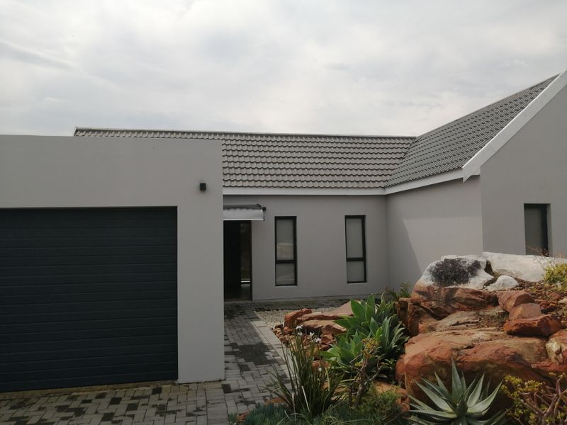 Front elevation of a modern house featuring a tiled roof, integrated garage, paved driveway, and a landscaped rockery garden.