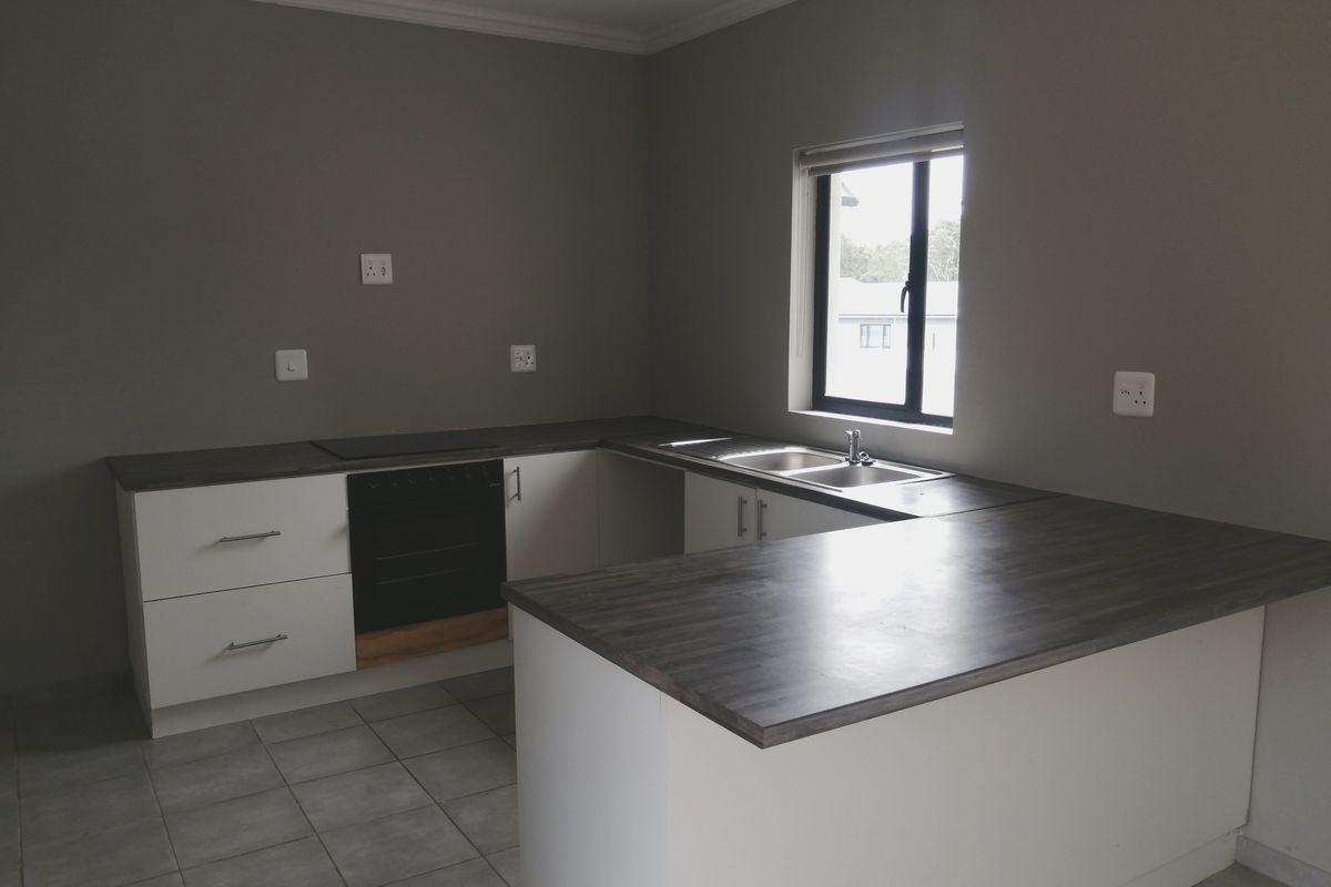 A clean, modern kitchen featuring white cabinetry, dark laminate countertops, a built-in oven, hob, and a double sink with tiled flooring.