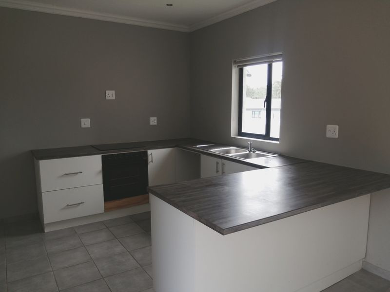 A clean, modern kitchen featuring white cabinetry, dark laminate countertops, a built-in oven, hob, and a double sink with tiled flooring.