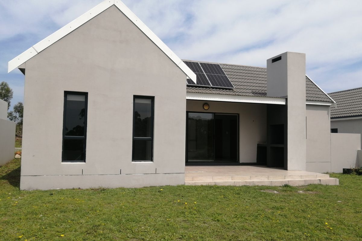 Rear view of a modern house featuring a tiled patio with a built-in braai, sliding doors, and roof-mounted solar panels.