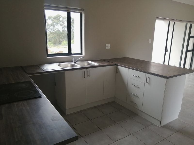 A clean, modern kitchen featuring laminate countertops, built-in cabinetry, an electric hob, and a stainless steel double sink with tiled flooring.