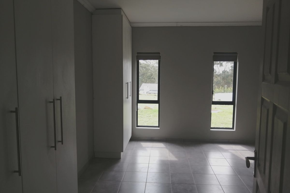A bright, empty bedroom featuring neutral tiled flooring, built-in cupboards, and dual windows with roller blinds.