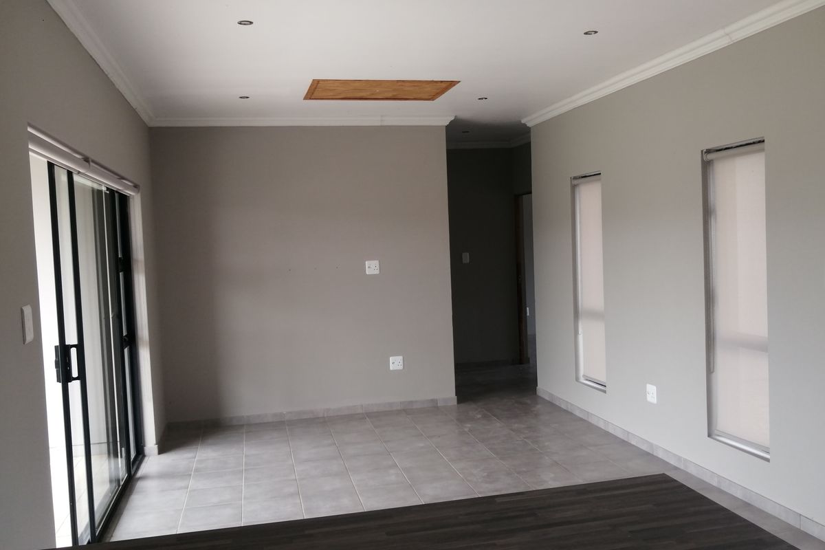 An empty, neutral-toned living area featuring tiled floors, recessed lighting, and a sliding glass door providing access to the exterior.