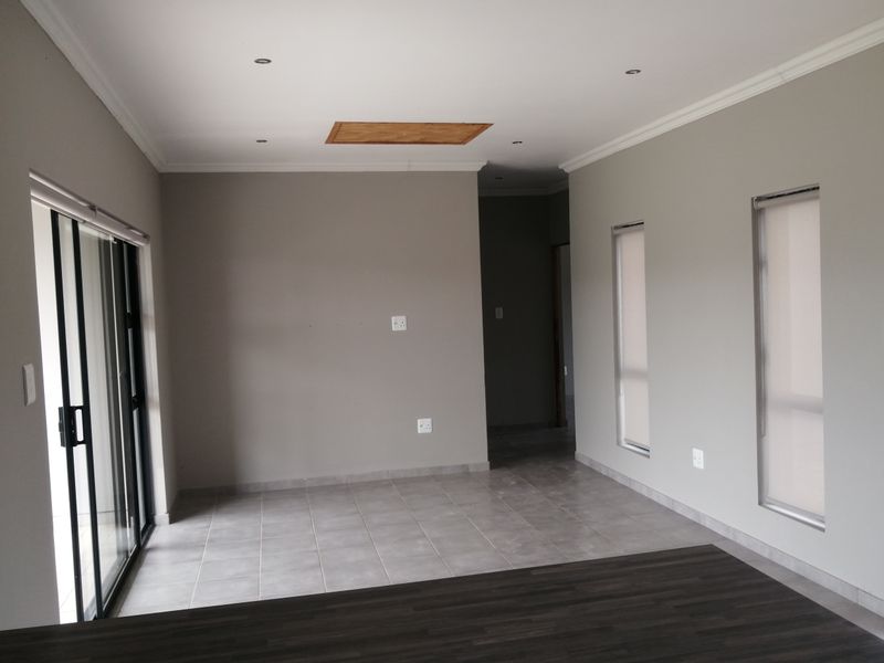 An empty, neutral-toned living area featuring tiled floors, recessed lighting, and a sliding glass door providing access to the exterior.