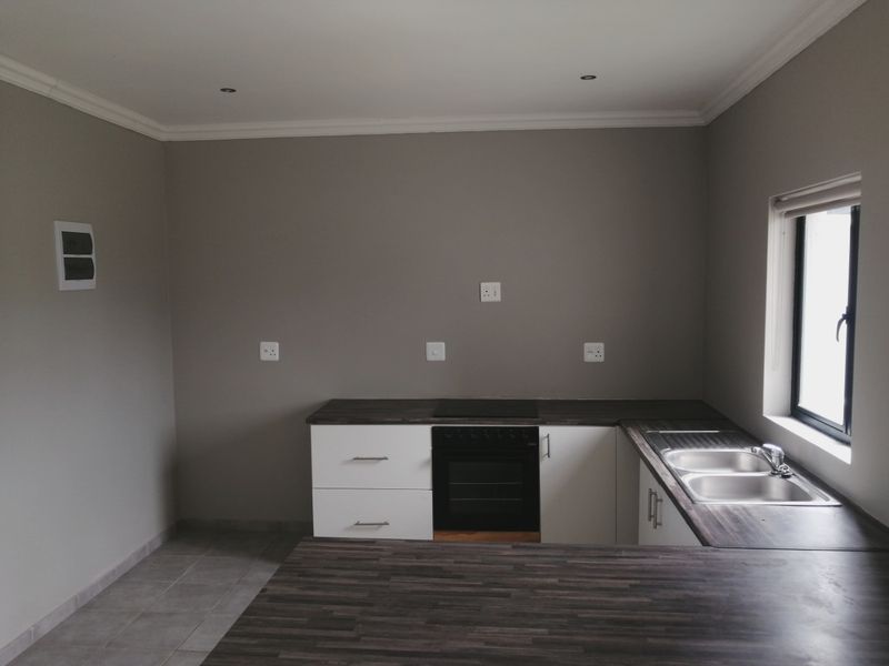 A clean, modern kitchen featuring built-in oven, electric hob, double sink, and ample laminate countertop space with neutral grey walls.