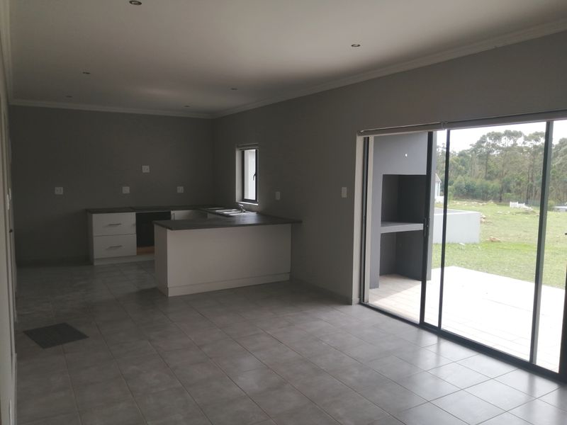 Open-plan kitchen and living area featuring modern cabinetry, tiled floors, and large sliding doors leading to an outdoor patio with a built-in braai.