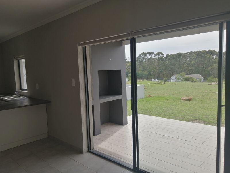 Open plan living area featuring a kitchen with countertop and sink, leading through sliding doors to a tiled patio with a built-in braai.