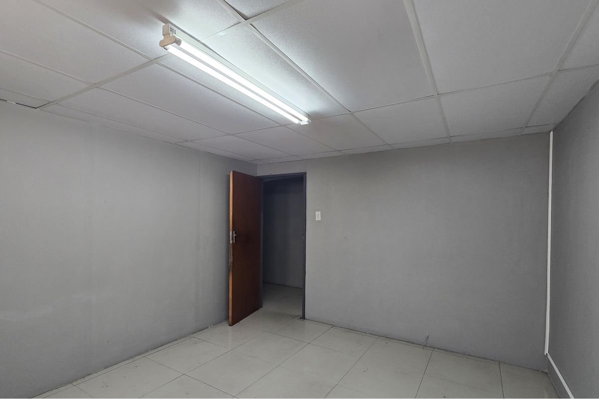 An empty, neutral-toned room featuring tiled flooring and a suspended ceiling, suitable for use as a bedroom or home office.