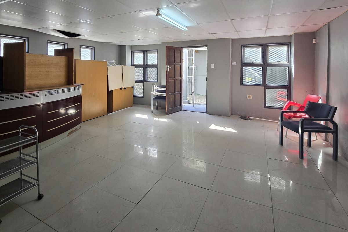 An open-plan interior space featuring tiled flooring, a drop ceiling, and security-barred windows, suitable for a variety of commercial or residential uses.