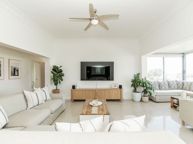 Spacious living room featuring polished tile floors, a modern ceiling fan, crown molding, and large sliding glass doors providing natural light.