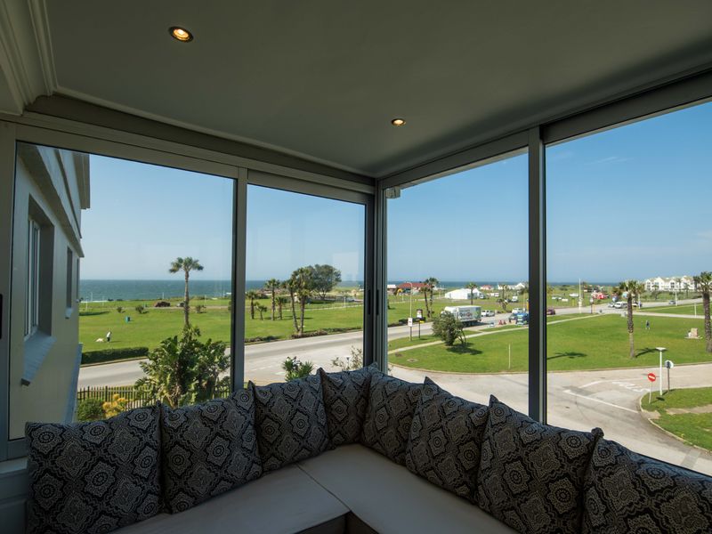 Enclosed balcony area featuring expansive glass windows offering panoramic coastal and park views, complete with built-in corner seating and recessed lighting.