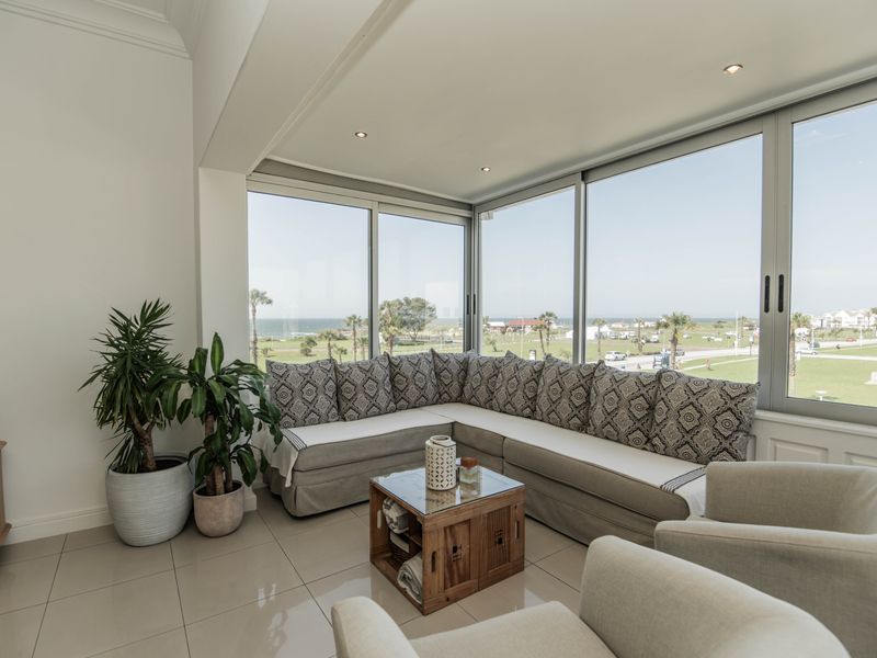Bright living area featuring large floor-to-ceiling windows with scenic coastal views, tiled flooring, and recessed lighting.