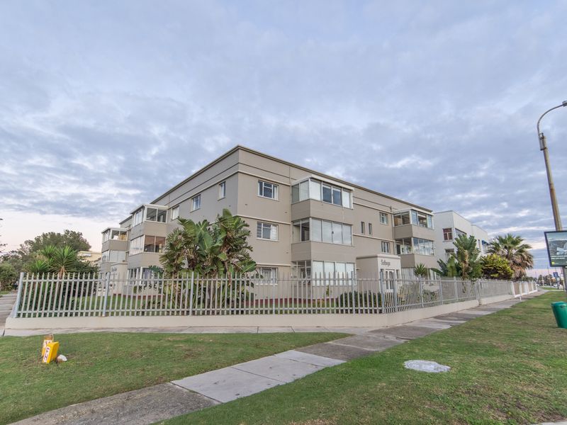 Exterior view of a multi-story apartment building featuring enclosed balconies and secure metal perimeter fencing.