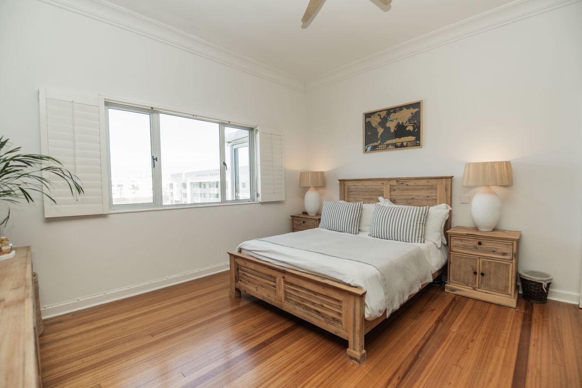 A well-maintained bedroom featuring polished timber flooring, a ceiling fan, and plantation shutters, offering a bright and comfortable living space.