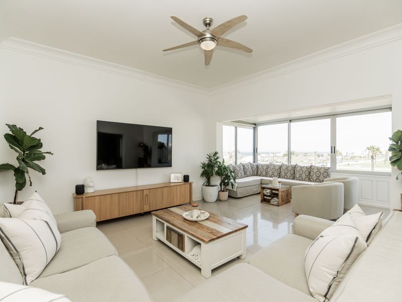 A bright and modern living room featuring tiled flooring, a ceiling fan, and large sliding glass doors that provide ample natural light.