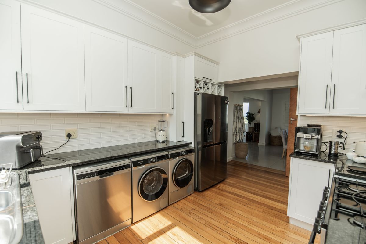 Modern kitchen featuring white shaker cabinetry, black granite countertops, subway tile backsplash, hardwood flooring, and integrated stainless steel appliances.