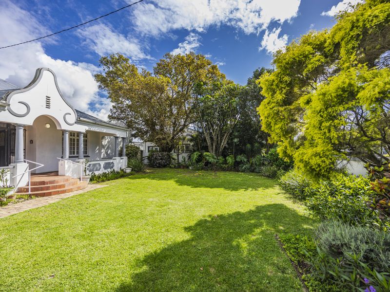 A well-maintained front garden featuring a classic Cape Dutch gable architectural style, a tiled entrance porch, and established landscaping.