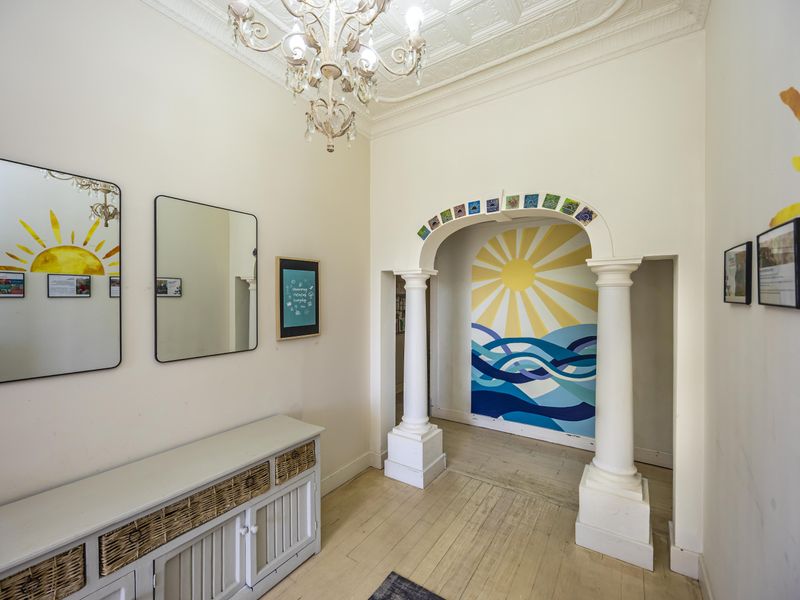 A bright entrance hall featuring classical columns, an arched doorway, ornate ceiling detailing, and polished timber flooring.