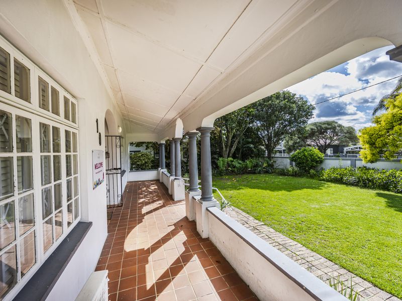 A covered veranda featuring terracotta tiling and classic columns, overlooking a well-maintained garden and lawn area.