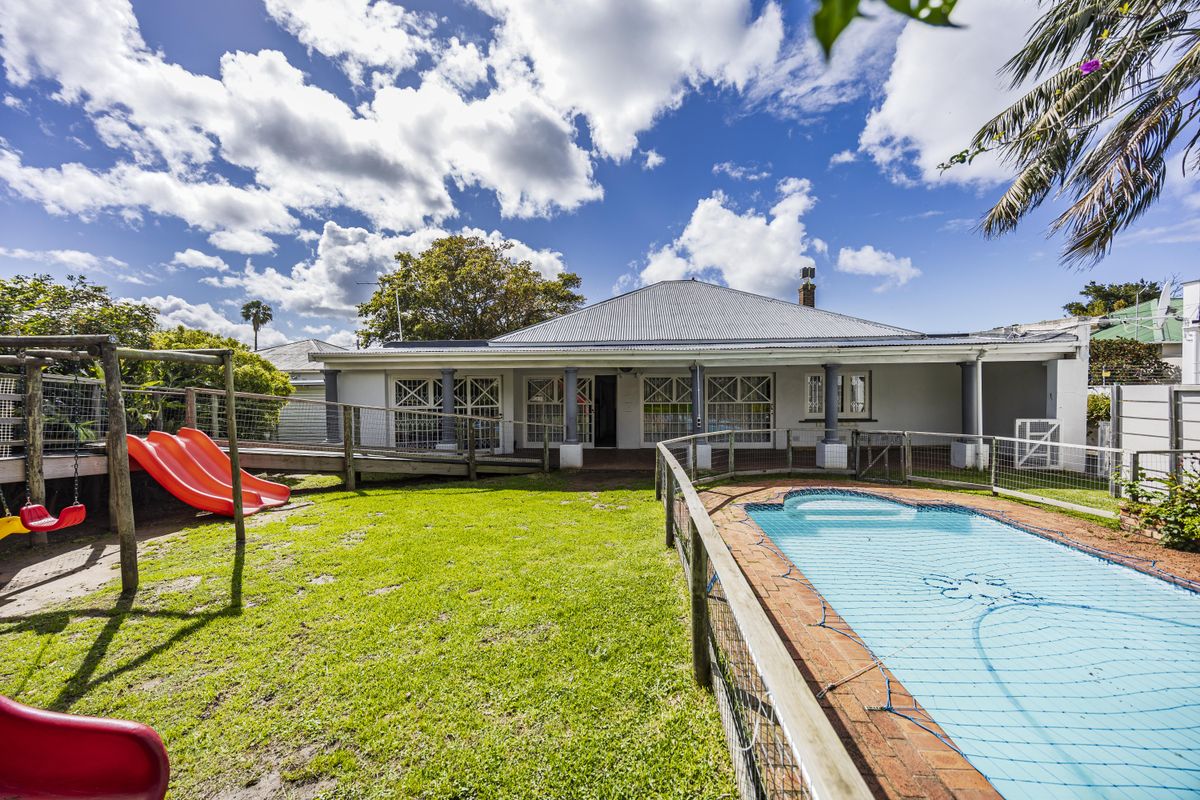 Rear view of the property featuring a covered patio, swimming pool with safety net, and a spacious lawn area.