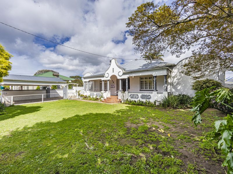 A charming single-story home featuring a gabled facade, covered front porch, and an adjacent carport, set within a spacious front garden.