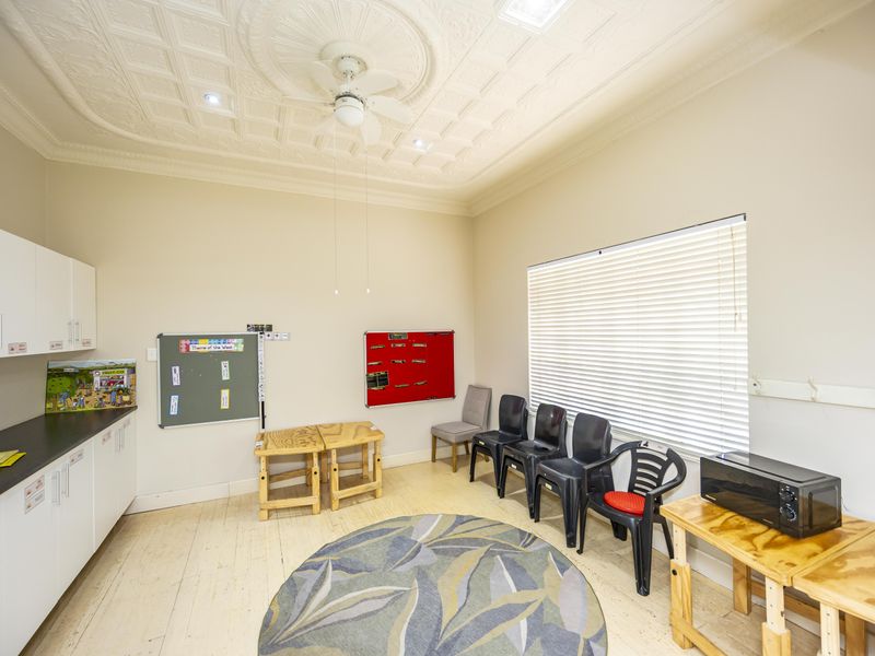 A functional utility space featuring built-in cabinetry, a decorative ceiling rose with a fan, and large windows with venetian blinds.