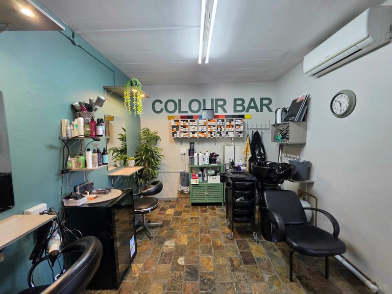 A functional utility space currently utilized as a salon colour bar, featuring stone tile flooring, a wash basin, and a wall-mounted air conditioning unit.