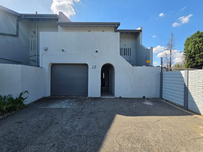 Front elevation of a townhouse featuring a single roller garage door, arched entrance, and paved driveway with perimeter security fencing.