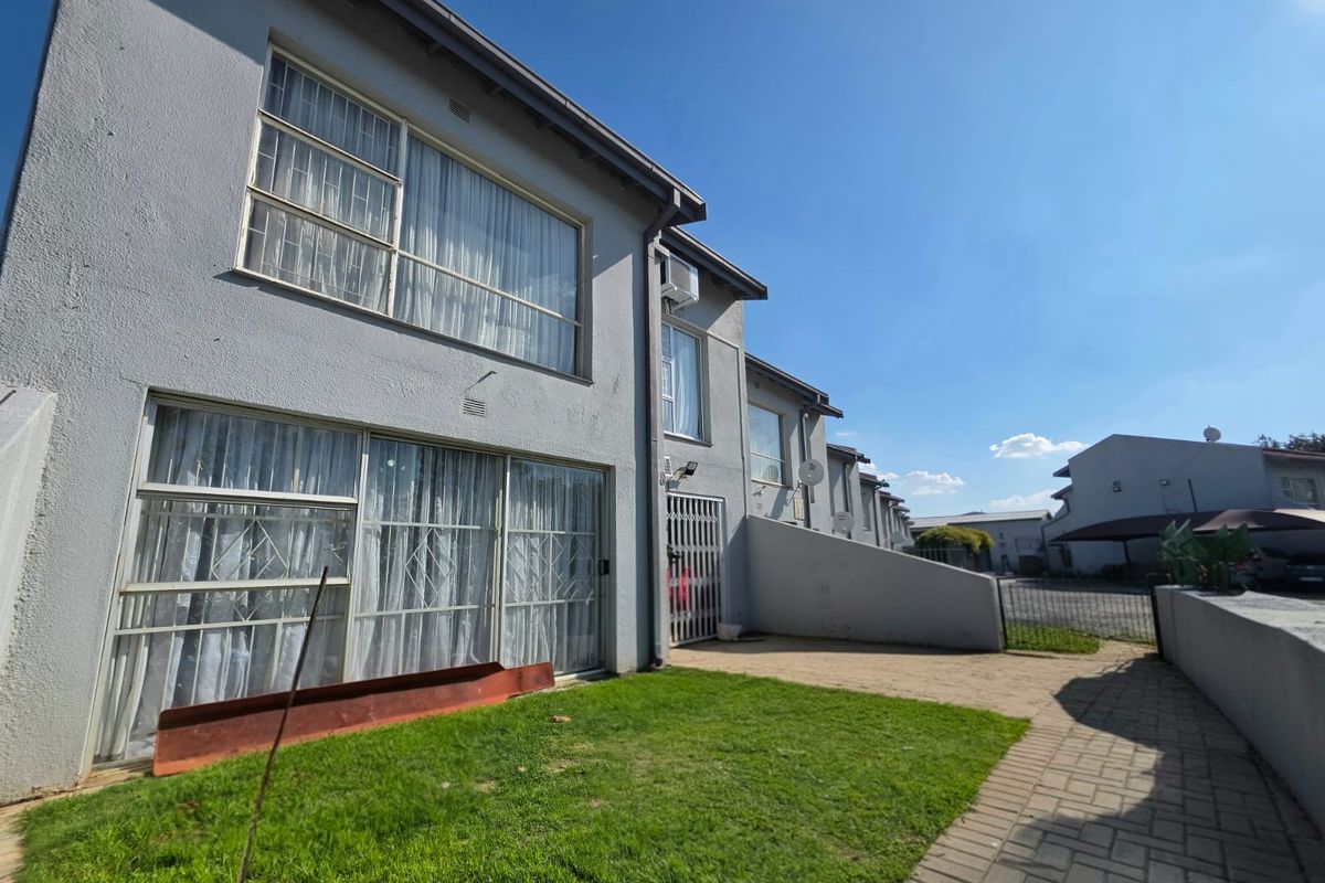Rear view of the townhouse featuring a small private lawn, paved walkway, sliding glass doors with security gates, and an exterior air conditioning unit.