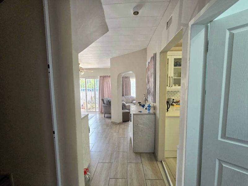 A view through a hallway connecting the living area and kitchen, featuring tiled flooring and an arched transition.