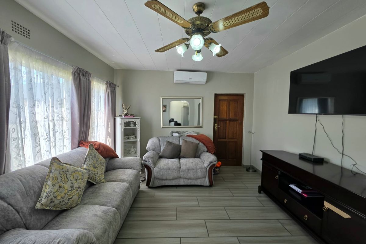 A comfortable living room featuring tiled flooring, a ceiling fan, and a wall-mounted air conditioning unit.