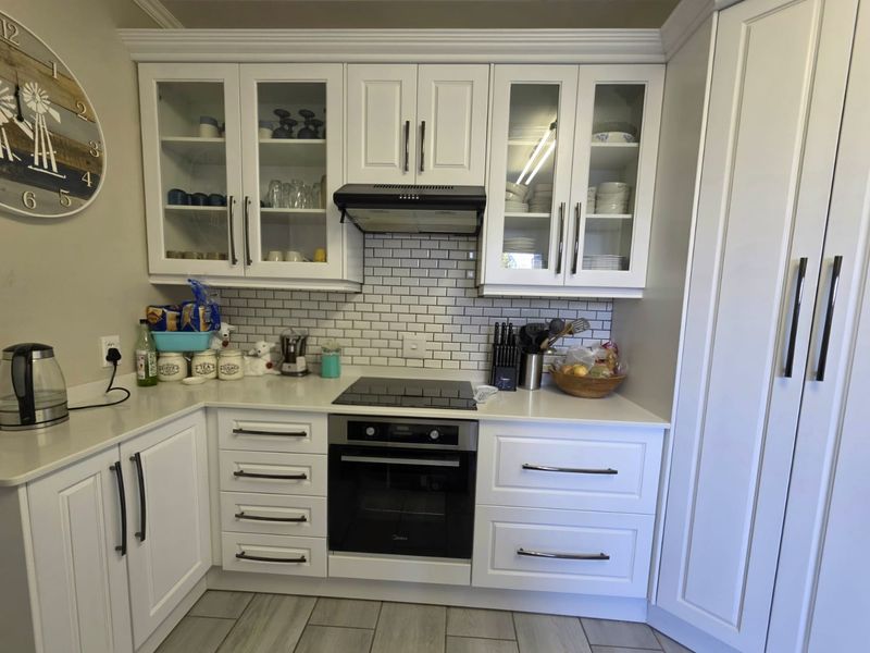 A well-maintained kitchen featuring white shaker-style cabinetry, subway tile backsplash, quartz countertops, and integrated appliances including an oven and electric cooktop.