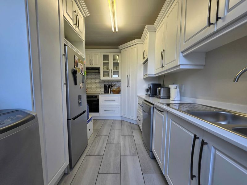 A well-maintained galley kitchen featuring white shaker-style cabinetry, subway tile backsplash, integrated appliances, and modern wood-look laminate flooring.