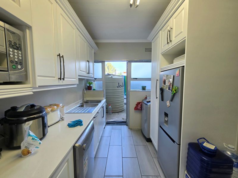 A functional scullery featuring white built-in cabinetry, a double sink, and tiled flooring, with direct access to the exterior area.