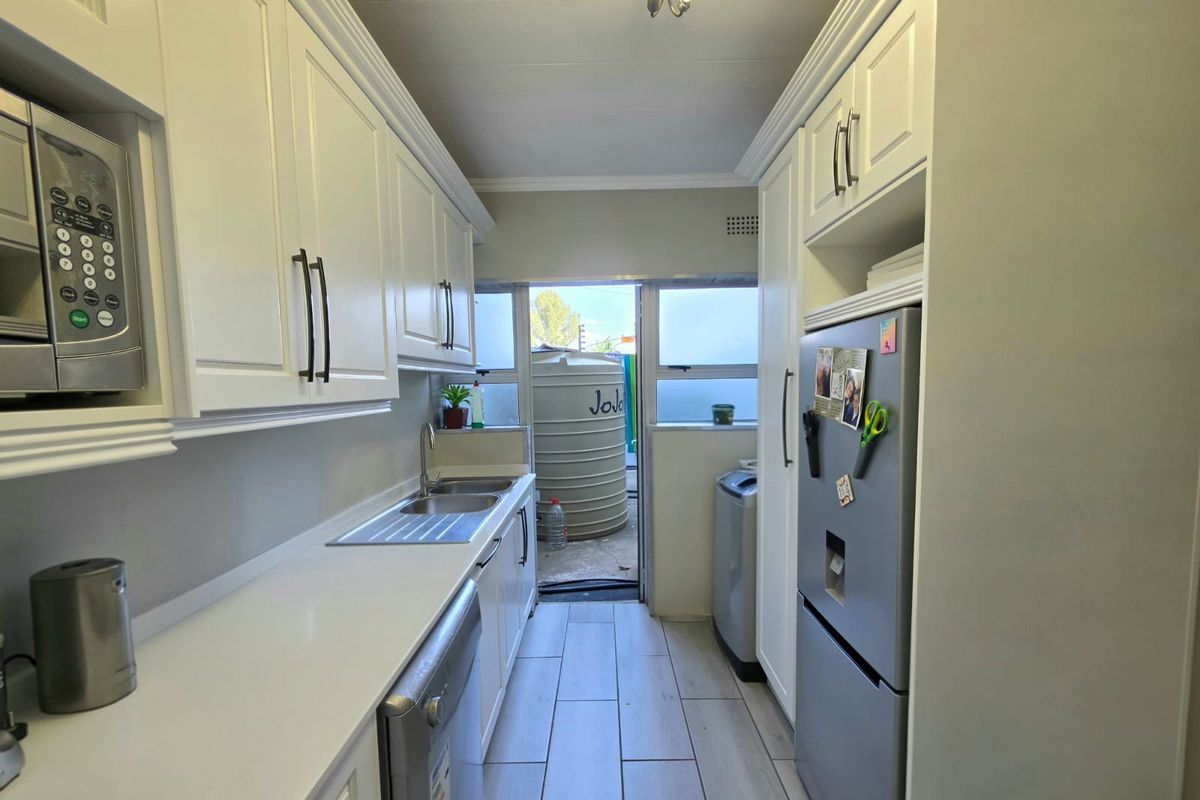 A clean, modern galley-style kitchen featuring white cabinetry, integrated microwave, stainless steel sink, and tiled flooring with direct access to the rear exterior.